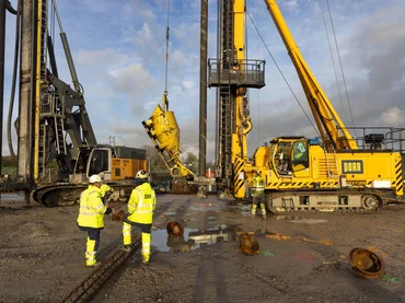 The picture shows a pile driver. In front of it stands a construction worker.